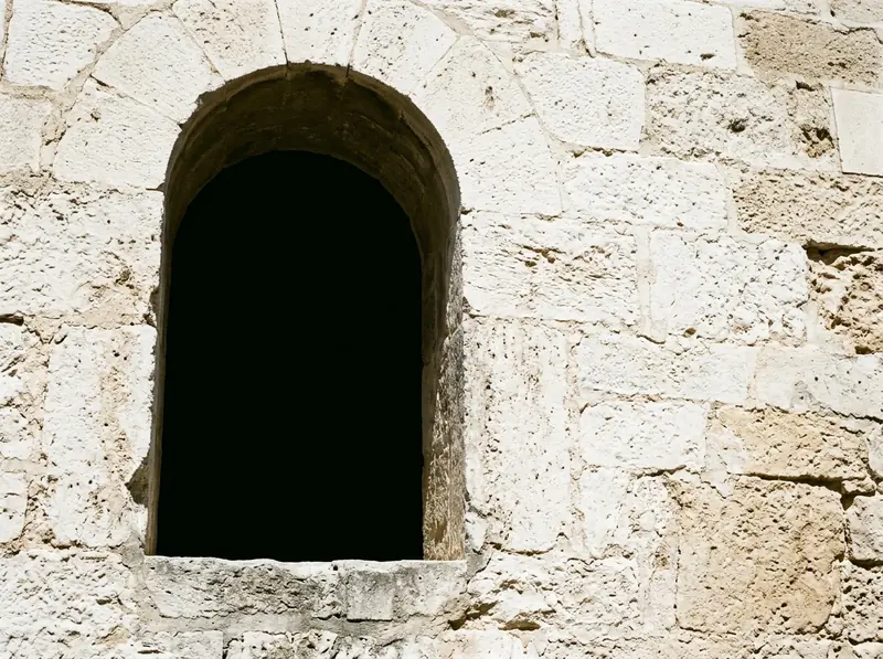 A deep set opening in pale masonry under harsh midday sun