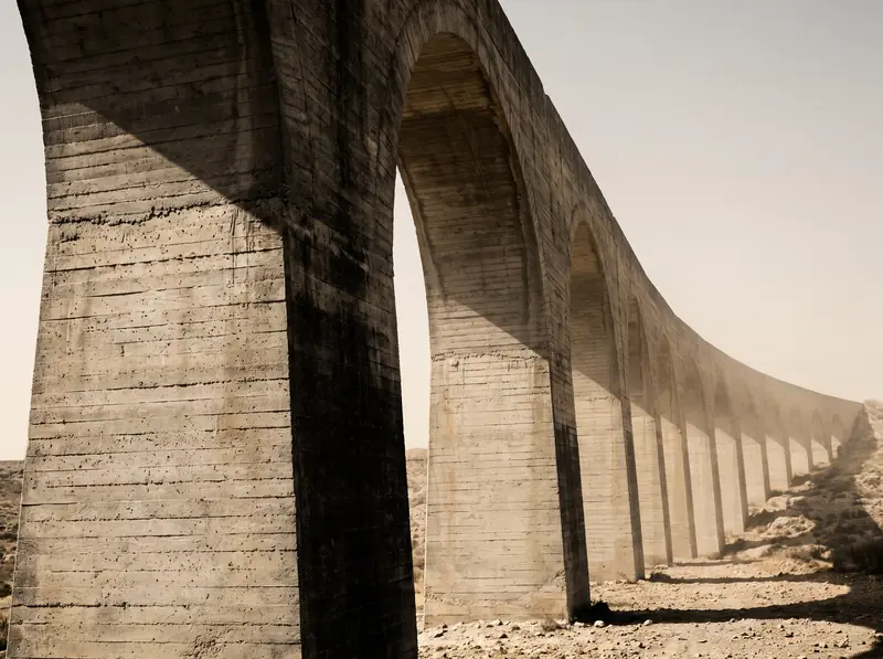 A modern concrete aqueduct crossing dry terrain, its arches repeating into pale dust haze
